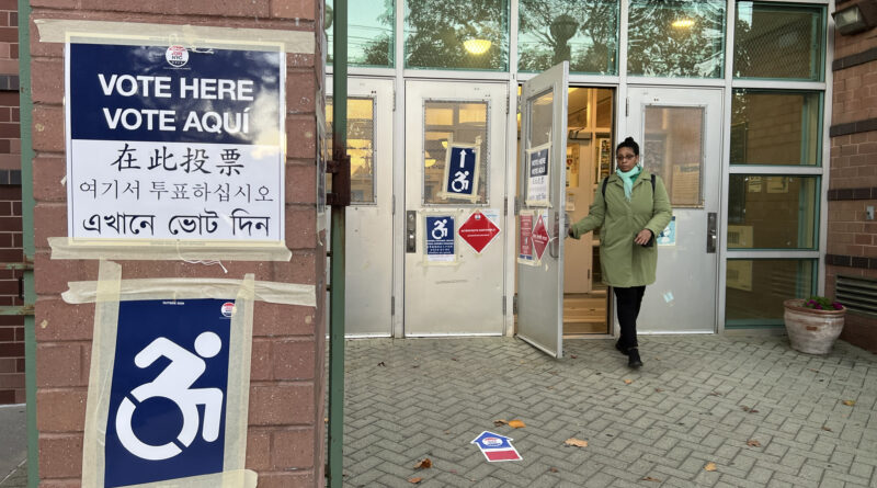 A woman in a green coat exiting a polling station with a version of the international symbol of access in view.