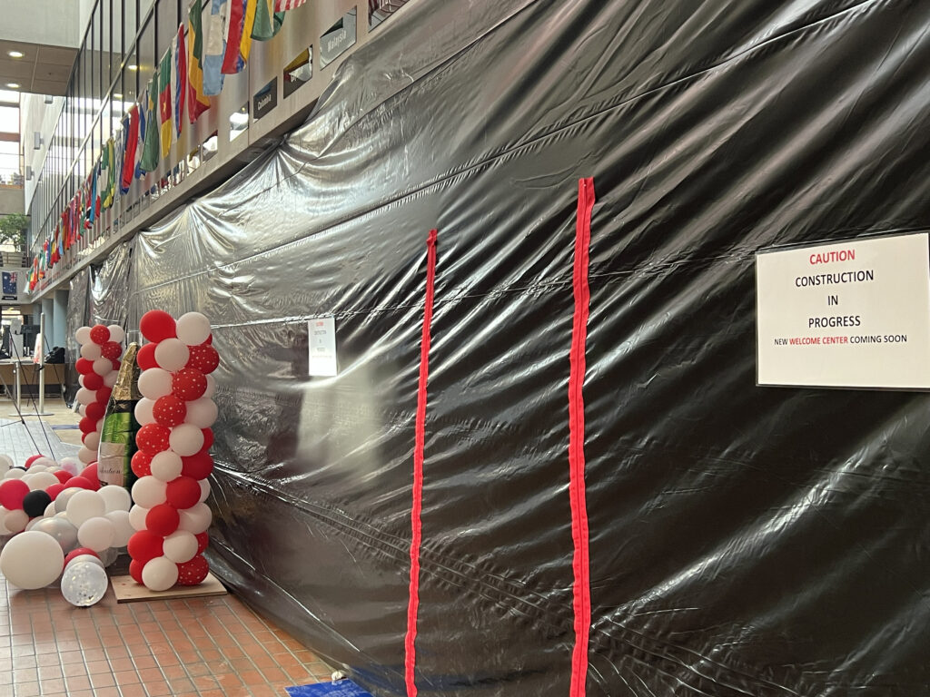 A black plastic covers the main entrance with a Caution Construction in Progress sign and balloons in the distance.