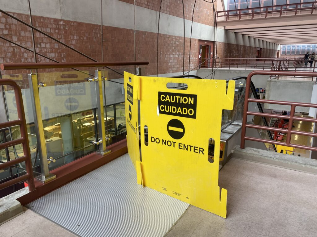 A broken escalator leading to the second floor with a yellow sign in front of it.